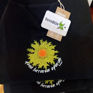 Sudadera oversize negra de mujer con eguzkilore verde lima y frase Ama lurraren opariak de ButtiBou Pamplona. Black oversized women's sweatshirt with green eguzkilore and phrase Ama lurraren opariak by ButtiBou Pamplona