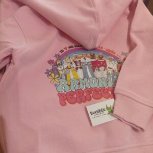 Sudadera infantil rosa con cremallera y capucha, diseño exclusivo “Gigantes en armonía” de ButtiBou Pamplona, inspirada en los gigantes de Pamplona. Pink children’s zip-up hoodie with hood, exclusive “Giants in Harmony” design by ButtiBou Pamplona, inspired by Pamplona’s giants.